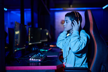 concentrated young woman wearing headphones while playing game in a blue lit room, cybersport