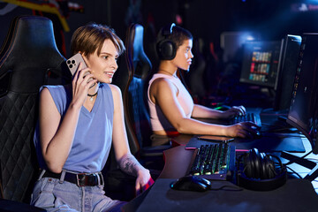 woman sitting at a computer desk talking by phone near friend playing in computer game in club