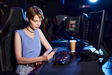 Fototapeta na wymiar short-haired woman using her smartphone near computer on desk, cybersport gamer in computer club