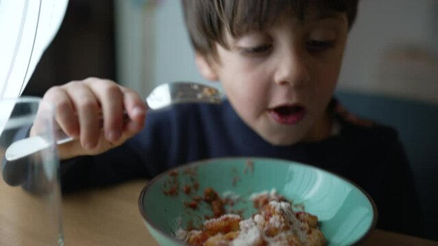 One little boy eating gnocchi on plate during mealtime. Close-up face of pensive 5 year old child holding fork enjoying food