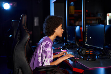 Fototapeta na wymiar curly african american gamer in headphones playing computer game while looking at screen, cybersport