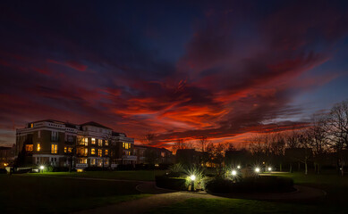 Park with lights at sunset with a fiery red sky. Night view in landscape orientation with buildings and trees behind.