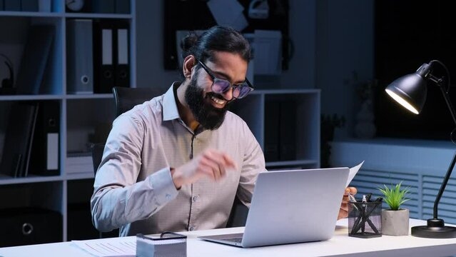 Thinking Indian entrepreneur working with documents and laptop, keeps business accounting, planning financial strategy, doing paperwork in late night office.