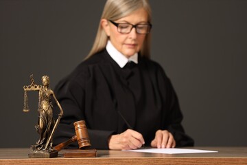 Judge working with document indoors, selective focus. Mallet and figure of Lady Justice on wooden table
