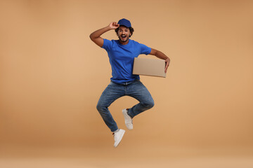 Fototapeta na wymiar Happy courier with parcel jumping on light brown background