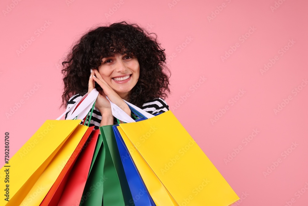 Wall mural Happy young woman with shopping bags on pink background