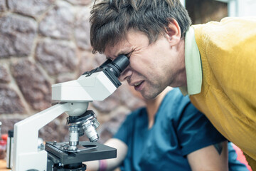 Man student or scientist examines specimen under microscope, observing intricate details.