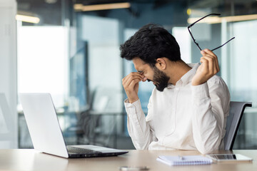 Exhausted indian businessman feeling stressed at work while sitting at his office desk