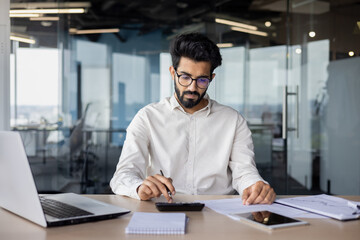 Obraz premium Focused indian businessman working on laptop in modern office - corporate professional concept