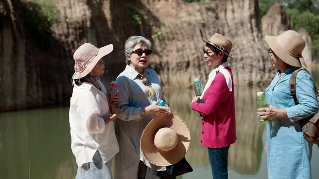 Best friends, group elderly Asian women have been close for long time, let's travel nature during day when sun is bright but weather is good, standing talking, resting, tired, holding water in hand.