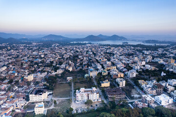 Fototapeta premium Aerial drone shot over udiapur, jaipur, kota,, cityscape with homes, houses, buildings and aravalli hills and lakes in the distance hidden in fog