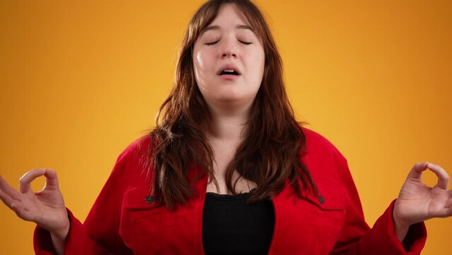 Brunette long hair young woman 20s in red jacket hold spreading hands in yoga om gesture relaxing meditating trying to calm down isolated on yellow background studio portrait