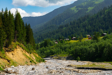 Picturesque view of wooden cottages on an alpine meadow and river bed while hiking Tour du Mont...