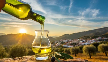 Schilderijen op glas Golden olive oil pouring amidst serene olive grove at sunrise, with mountain village silhouetted against colorful sky © Your Hand Please