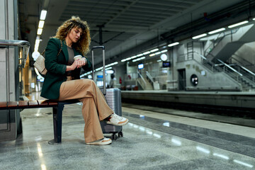 A weary businesswoman with curly hair sits, patiently awaiting her train at the station.