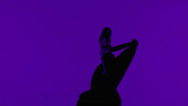 Woman dancer dancing on purple background. Female in flamenco style dress performs elegant spanish dance moves with her hands and body in the studio.