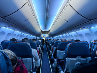 An airplane cabin with beautiful lighting and passengers sitting with their backs towards the camera - obrazy, fototapety, plakaty