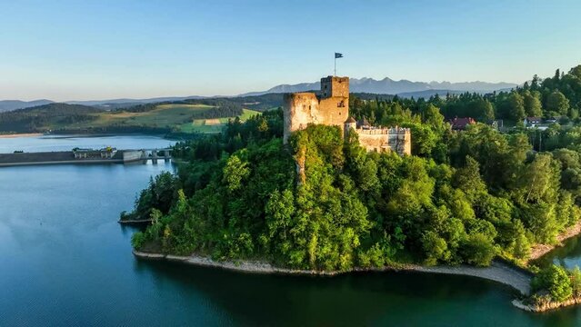 Poland. Medieval castle in Niedzica in sunset light. Artificial Czorsztyn lake on Dunajec river, dam and hydro power station,. Tatra Mountains in the background. Aerial approaching 4K video