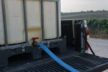 Pikup with tank, ready to fill with water. Blue hose plugged into the tank spout
