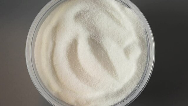 Glucono-delta-lactone, also known as gluconolactone. Pure GDL powder in plastic container, top view. Food additive E575. Acidity regulator, baking powder. 4K video, rotating.