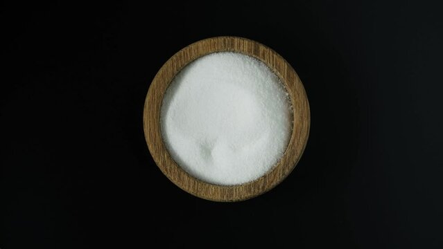Food additive E575 in wooden bowl, top view. Glucono-delta-lactone, also known as gluconolactone. Pure GDL, white odorless crystalline powder. Acidity regulator, baking powder. 4K video, Rotating.