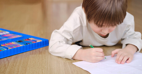 Creative child drawing with colored pencils on big white sheet, view from side