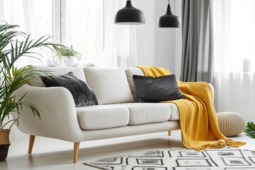 Scandinavian sofa with pillows and dark yellow blanket in bright living room interior with black chandelier.