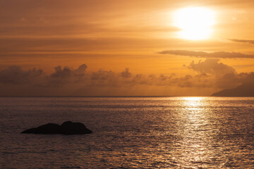 Seaside landscape, shore water and a rock under sunset sky. Seychelles