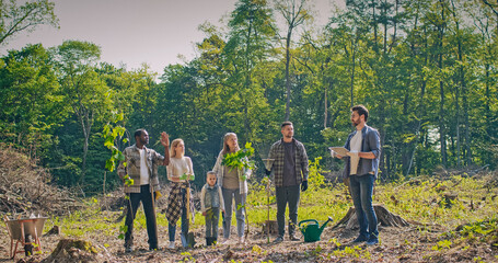 People of different ages planting trees in nice forest. Enthusiastic group of volunteers listening to leader and working together helping nature by growing more trees. Ecology concept.