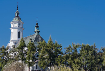 Piękny zabytkowy kościół kolegialny na wzgórzu wśród drzew  na tle intensywnie niebieskiego nieba Kilkusetletnia świątynia katolicka pod wezwaniem Świętego Michała Archanioła w Ostrowcu Świętokrzyskim