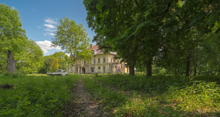Stary podupadły i zniszczony pałac - dawna siedziba magnackiego rodu Druckich- Lubeckich , stojący w zabytkowym parku . Wiosenne pogodne popołudnie pod błękitnym niebem wśród starych drzew.