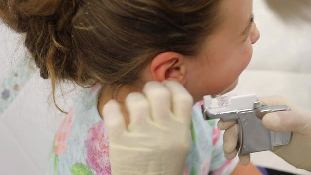 Doctor hands makes ear piercing to teenage girl, close up