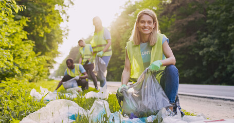 Portrait of cute young beautiful Caucasian woman picking up garbage taking part in volunteers...