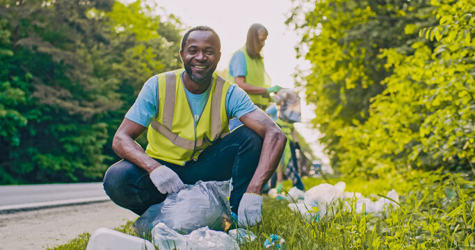 Portrait of Caring worker looking at camera with smile. African American man as part of team of enthusiastic volunteers cleaning up area near road saving nature from pollution.