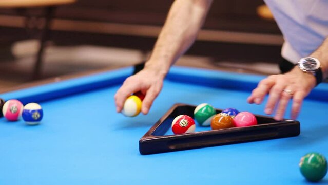 Male hands align balls with triangle during pool game on blue table, slow motion, noface