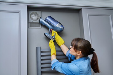 Woman cleaning wall-mounted hood ventilation grill in bathroom with vacuum cleaner