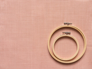 Flat lay of accessories for hand embroidery - two types of wooden hoops on special pink canvas with...