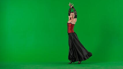 Woman dancer dancing on chroma key green screen. Female in flamenco style dress performs elegant spanish dance moves with her hands and body in the studio. - obrazy, fototapety, plakaty