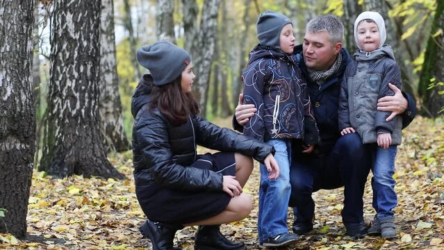 Father with two sons and one daughter squatting in autumn forest, slow motion