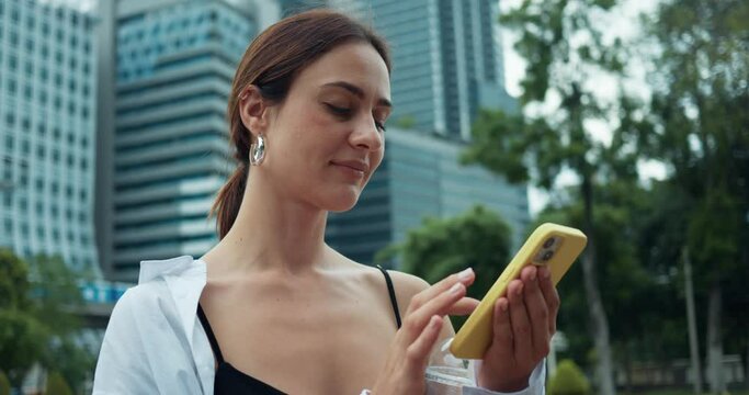 In Bangkok woman holds glass of water uses phone towering modern skyscrapers behind. Bangkok where tradition meets futuristic architecture Bangkok hub of new technology heart of Thailand.