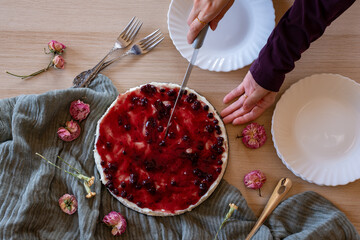 hands slicing cheesecake on wooden background with roses around