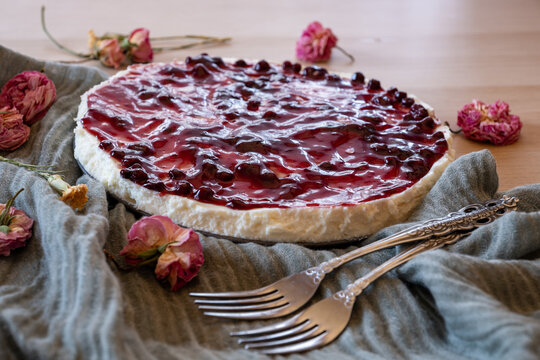 Cold cheesecake with cherry jelly and roses around it served on wooden background with green throw and antique forks