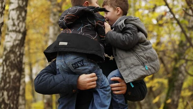 Close-up of handsome man holding two sons in his arms in an autumn forest with shallow depth of field, slow motion