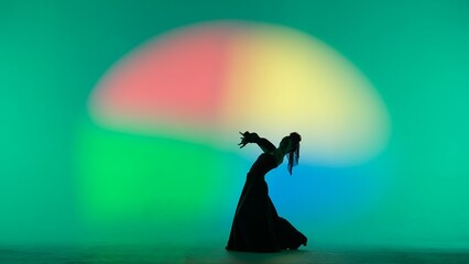 Woman dancer silhouette dancing on colorful background. Graceful dancer passionately dancing flamenco performing elements of Spanish style choreography.