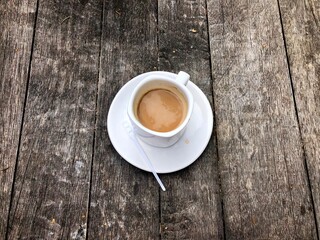 White cup of coffee and a white plate on a rustic wooden table