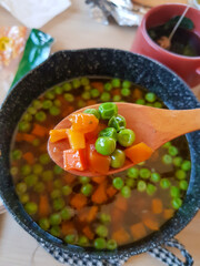 Wooden spoon holding sip of soup consist of carrots and peas