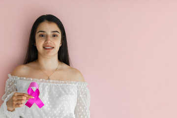 latina woman smiling while holding a pink ribbon symbolizing breast cancer on a light pink background