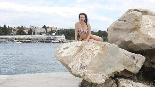 Happy woman in swimsuit poses on big stone on sea shore in Split, Croatia