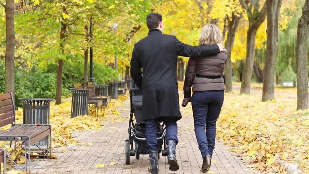 Woman and man go with baby carriage in fall park, slow motion, back view