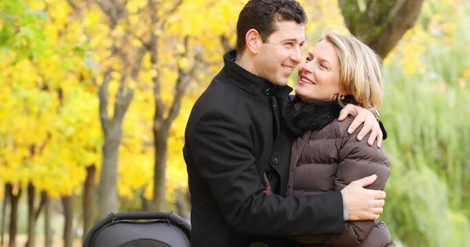 Handsome man embraces woman near baby carriage in fall park